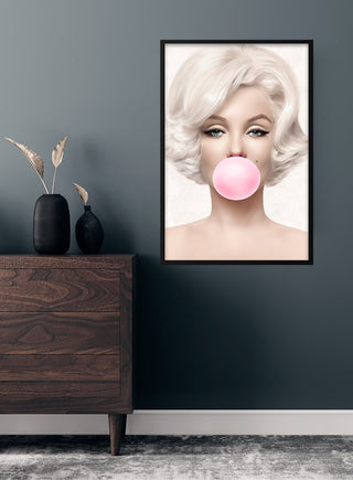 Poster of Marilyn Monroe blowing pink bubblegum, displayed on a wall above a wooden dresser.