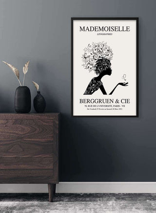 Framed "Mademoiselle Exhibition #1" poster on a wall above a modern dark wood dresser with minimalist decor.