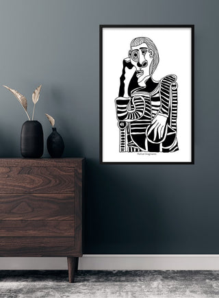 Picasso inspired Portrait imaginaires poster in black and white, framed on a modern dark wall above wooden furniture.