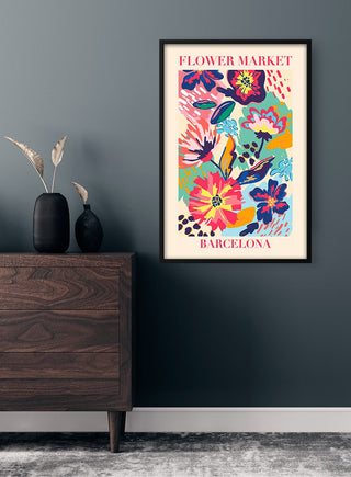 Framed "Flower Market Barcelona" poster with colorful floral design, displayed on a dark wall above a wooden dresser.