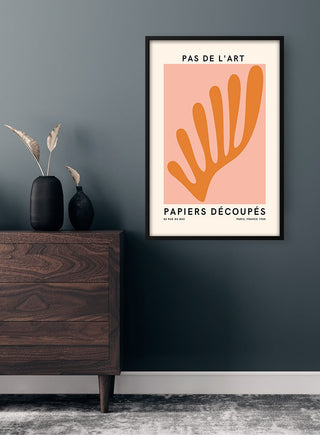 Framed Pas De L'art French art plakat with abstract orange cut-out pattern displayed above a wooden dresser.
