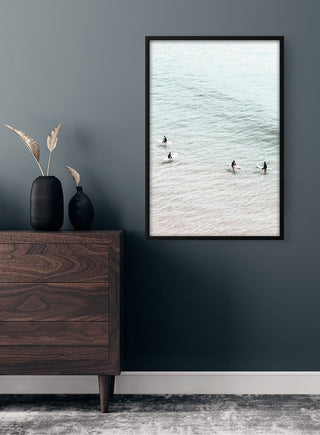 Framed "Surfers in Water" poster on a dark wall above a wooden dresser with vases.
