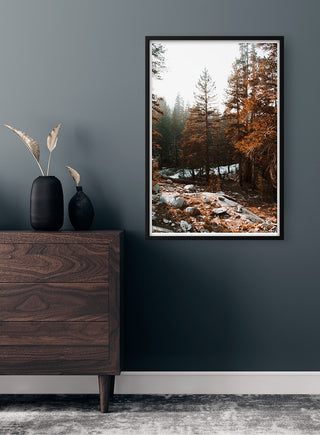 Framed autumn trees poster with orange foliage hanging on a dark wall above a wooden dresser.