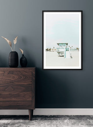 Framed Beach Tower Naturposter on a gray wall above a wooden dresser with vases and dried plants.