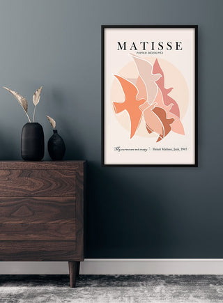 Framed Matisse Inspired Birds II Plakat featuring abstract bird shapes in warm tones, displayed on a dark wall.