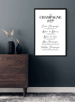 Framed "The Champagne Guide" poster hanging on a gray wall above a wooden dresser with vases.
