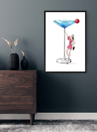 Framed "I Need a Drink - Vincent V." art print on wall, showing woman in pink beside large blue cocktail.