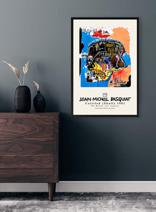 Framed "Skull" by Jean-Michel Basquiat displayed on a dark wall above a wooden dresser with decor.