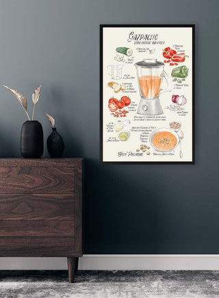 Framed Spanish illustrated Gazpacho recipe poster with vegetable drawings and blender, displayed on a dark wall.