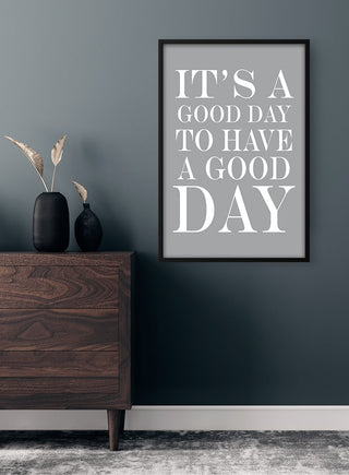 Framed "It's a Good Day to Have a Good Day" quote poster on dark wall above wooden dresser.