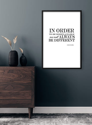 Framed "Be Different" quote poster on a gray wall above a modern wooden dresser with black vases.