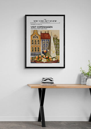 Framed Copenhagen art poster featuring colorful buildings and fruit, hung above a wooden desk with decor.
