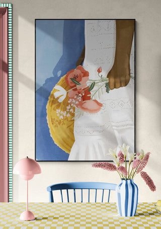 Art print of a hand holding pink flowers, hung above a table with a striped vase and pastel decor.