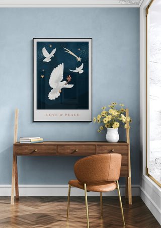 Framed "Love a Peace - Goed Blauw" poster with doves displayed above a wooden desk in a stylish room.