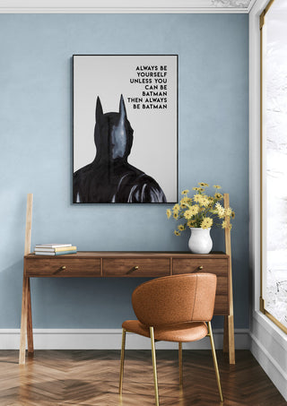 Framed Always Batman - Daniel Leo artwork above a wooden desk with books, vase, and yellow flowers in a modern room.