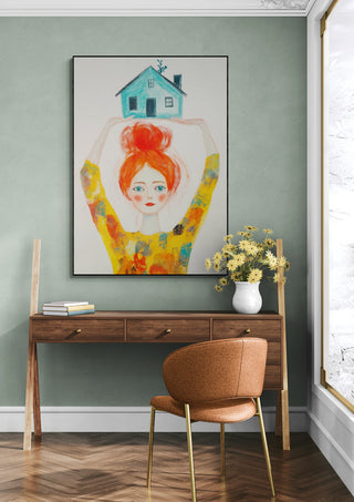 Framed "Strong as Pippi" artwork by David Wolf hangs above a modern desk with flowers and a chair.