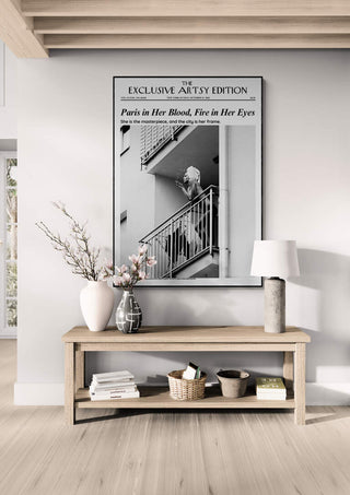 Framed Paris In Her Blood Artsy Edition poster above a wooden console with decorative vases and baskets.