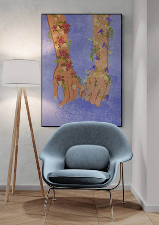 Framed artwork of two hands holding, adorned with floral patterns, displayed above a modern chair and lamp.