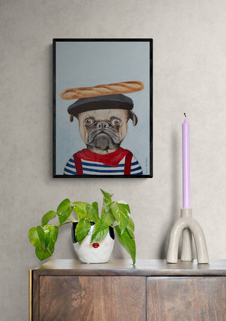 Framed artwork of a French pug in a beret and striped shirt with baguette, displayed above a cabinet.