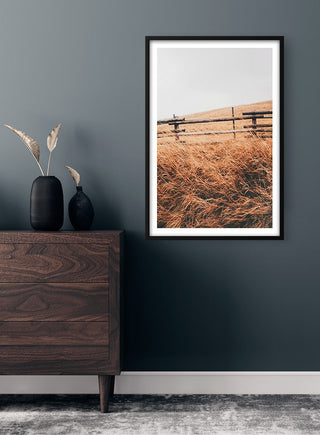 Framed Autumn Field Naturposter with tall golden grass and rustic fence, displayed above a wooden dresser.