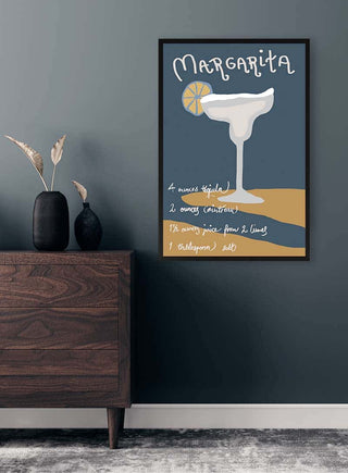 Framed Margarita recipe art print on a dark wall above a wooden dresser with minimalist decor.