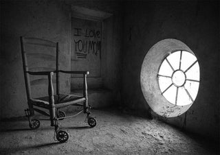 Black and white photo of The chair by Giorgio Toniolo in an empty, dimly lit room with a round window.