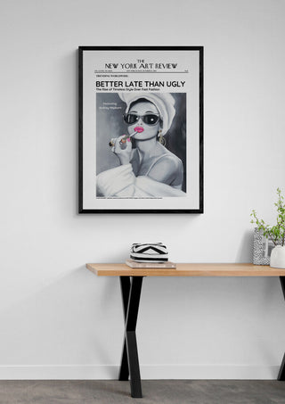 Framed "Audrey - Art Review Plakat" poster on a white wall above a wooden table with small decor items.