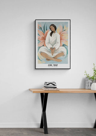 Framed Grace in the Meadow - Elara Monet art print on a white wall above a wooden desk with plants.