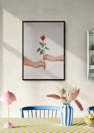 Framed print of two hands exchanging a single red rose, displayed above a dining table with flowers.