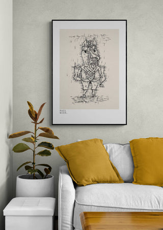 Framed print of "Ass Esel 1925" by Paul Klee hanging above a sofa with yellow pillows and a potted plant.