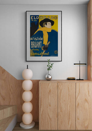 Framed "Les Ambassadeurs Aristide Bruant - Lautrec" poster displayed above a modern wooden cabinet in a stylish room.