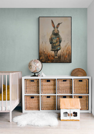 Framed Fashion Show Rabbit art above a wicker cabinet in a cozy, modern nursery room.