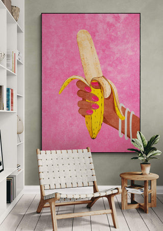 Large artwork by Raissa Oltmanns of a hand holding a banana, displayed on a wall above a chair.